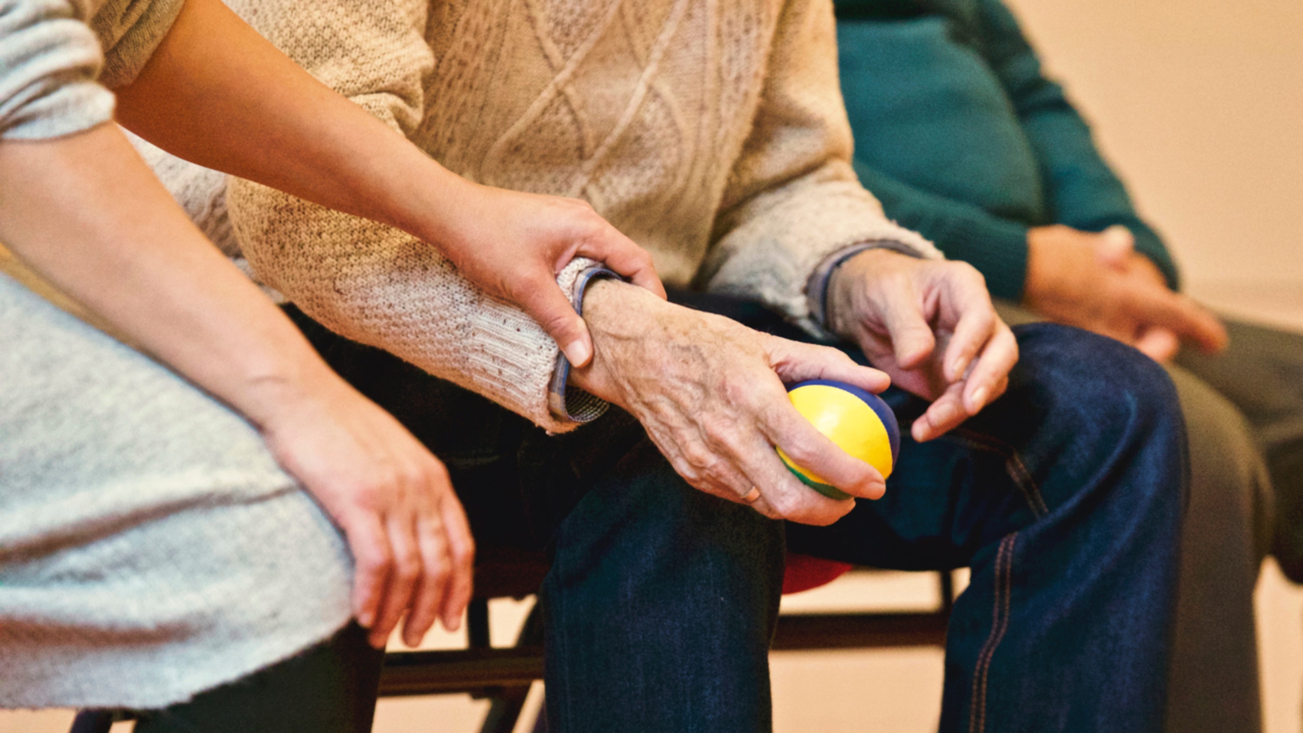 main d'une personne adulte tenant la main d'une personne âgée, qui tient une balle dans sa main